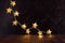 Luxury home decor for New Year party - stripe of gold Christmas glowing lights with stars in elegant dark interior on brown wood.