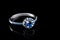 Luxury jewellery. White gold or silver engagement ring with colored gemstone closeup on black background. Selective focus.