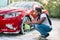 Luxury red car in soap foam outdoors at car wash service. Side view of handsome young African man using green microfiber