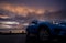 Luxury SUV car with raindrops. Front view new blue SUV car parked on concrete parking lot near sea beach with sunset sky. Electric