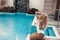 Luxury travel bikini blonde girl with sexy body in white swimwear posing by swimming pool at luxurious villa. Fashion colors,