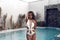 Luxury travel bikini girl with sexy body in white swimwear posing by swimming pool at luxurious villa. High fashion colors,