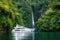 luxury yacht anchored in serene lagoon, with waterfalls and lush greenery visible in the background