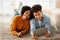 Lying on a shaggy rug, a cheerful young couple shares a tablet, their laughter