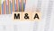 M and A word written on wood block. Faqs text on table, concept