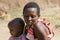 Maasai woman with her unidentified baby rest in the savannah.