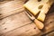 Maasdam cheese with a cheese fork on a dark cutting board on aged wood background, selective focus