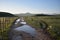 The macadam road dotted with the puddles and the mountains at the background