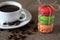 Macaron three pieces red, green and orange tied with rope and mug with coffee, scattered beans and saucer on burlap tablecloth