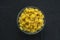 Macaroni ruote pasta in a glass bowl on a black textured background, in the center close-up from the top.