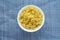 Macaroni ruote Pasta in a white cup on a blue knitted background in the center. Close-up with the top.