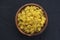 Macaroni ruote pasta in a wooden bowl on a black textured background, in the center close-up from the top.