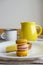 Macaroons and lemon tart on white plate. Whine enamel mug, yellow ceramic jug. Still life in pastoral style aesthetics.