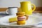 Macaroons and lemon tart on white plate. Whine enamel mug, yellow ceramic jug. Still life in pastoral style aesthetics.