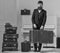 Macho elegant on strict face stands near pile of vintage suitcase, holds suitcase. Man, traveller with beard and