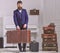 Macho elegant on strict face stands near pile of vintage suitcase, holds suitcase. Man, traveller with beard and