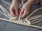 Macrame. Girl weaves macrame. White thread, female hand, grey background, close-up