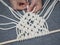 Macrame. Girl weaves macrame. White thread, female hand, grey background, close-up