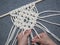 Macrame. Girl weaves macrame. White thread, female hand, grey background, close-up