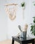 Macrame tapestry hanging above weaving tools and materials on a stool