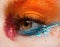 Macro and close-up creative make-up theme: Beautiful female eye with red and blue sparkles and orange pigment