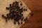 Macro close-up of Organic Black pepper Piper nigrum on wooden top background and jute mat. Pile of Indian Aromatic Spice.