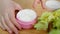 Macro finger takes cream from jar on table with greens