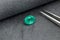 Macro mineral emerald stone with tweezers on gray fabric