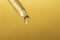 Macro of pipette with liquid and drop on gold background