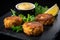 Macro shot of mini crab cakes served on a black slate with a side of mustard dipping sauce and lemon wedges
