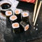 Macro shot of salmon hosomaki sushi on natural black slate plate background with selective focus. Thin maki sushi rolls with raw t