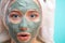 Macro shot of shoked surprised woman with clay facing mask and towel on face