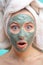 Macro shot of shoked surprised woman with clay facing mask and towel on face