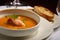 Macro shot of a small dish of lobster bisque soup with a slice of crusty bread and a sprig of parsley on the side