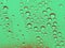 A macro texture photo of water drops on glass tinted green