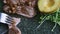 Macro view human hands cut off slice of grilled meat by fork and knife on black plate