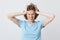 Mad crazy young woman in blue t shirt with hands on head and eyes closed standing and suffering from headache isolated over white