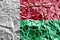 Madagascar flag depicted in paint colors on shiny crumpled aluminium foil closeup. Textured banner on rough background