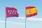 Madrid region and Spain flags on flag poles waving against sky background