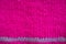 Magenta knitted horizontal textured winter background. Fragment of a bright pink color tied to the needles of a children`s sweate