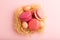 Magenta and pink macaroons and chocolate eggs in decorative paper nest on pink pastel background. top view, close up