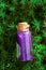 Magic Potion.Bottle with purple shiny glittering liquid in green moss on blurred green forest background.Magic and fairy