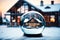 Magical glass ball with tiny modern house inside near big real cozy house with lights in windows in winter. Gift dream for