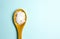 Magnesium Chloride Flakes scattered around brown wooden spoon on blue background.