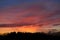 Magnificent evening sky with colorful orange and red clouds over silhouette of a forest in backlight.