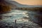 Magnificent landscape during the sunset. Adorable wedding couple is hugging in the middle of the river.