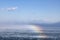 Magnificent rainbow arcs across a stunning blue sky above a vast expanse of the azure ocean