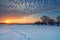 Magnificent sunset over snow covered field with winding footprints straight ahead to the sun