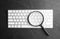 Magnifier glass and keyboard on black background, flat lay. Find keywords concept