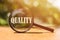 Magnifier glss with text QUALITY on wooden table in sunlight. Business concept